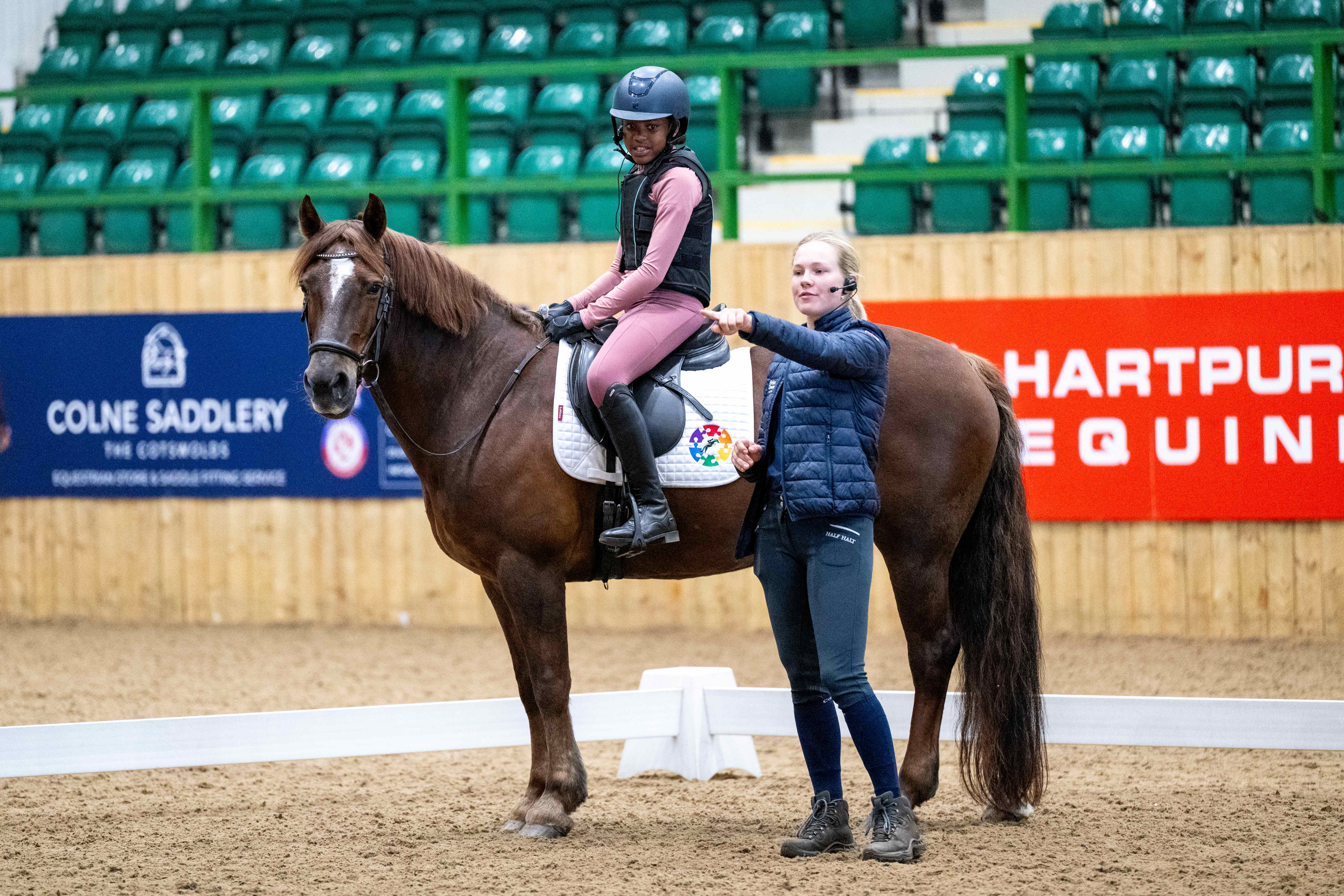 Coach pointing while smiling rider and chestnut pony watch.